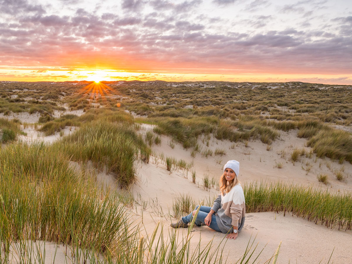 Frau sitzt beim Sonnenuntergang in einer Dünenlandschaft auf Texek