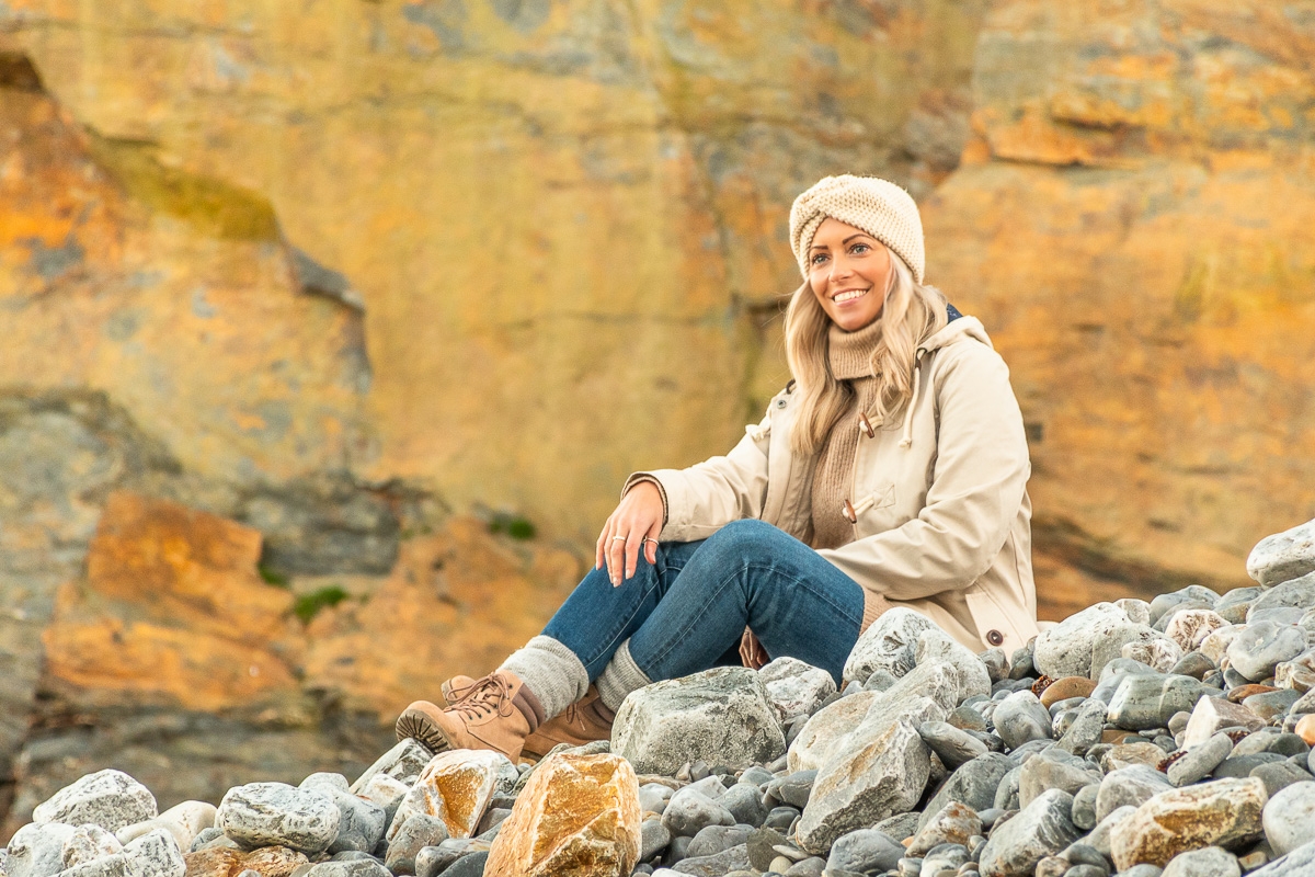 Frau sitzt vor einer hellen Steinwand am Meer