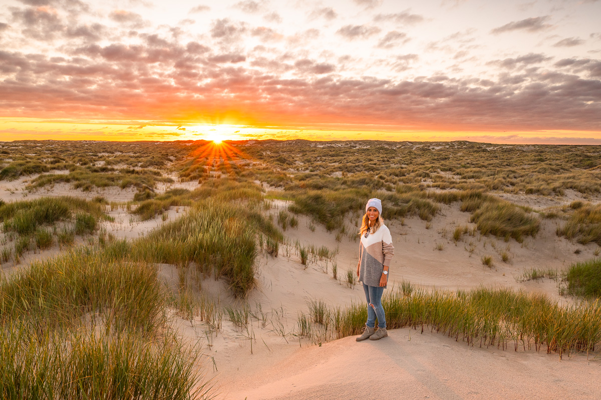 Frau steht beim Sonnenuntergang in den Dünen auf Texel