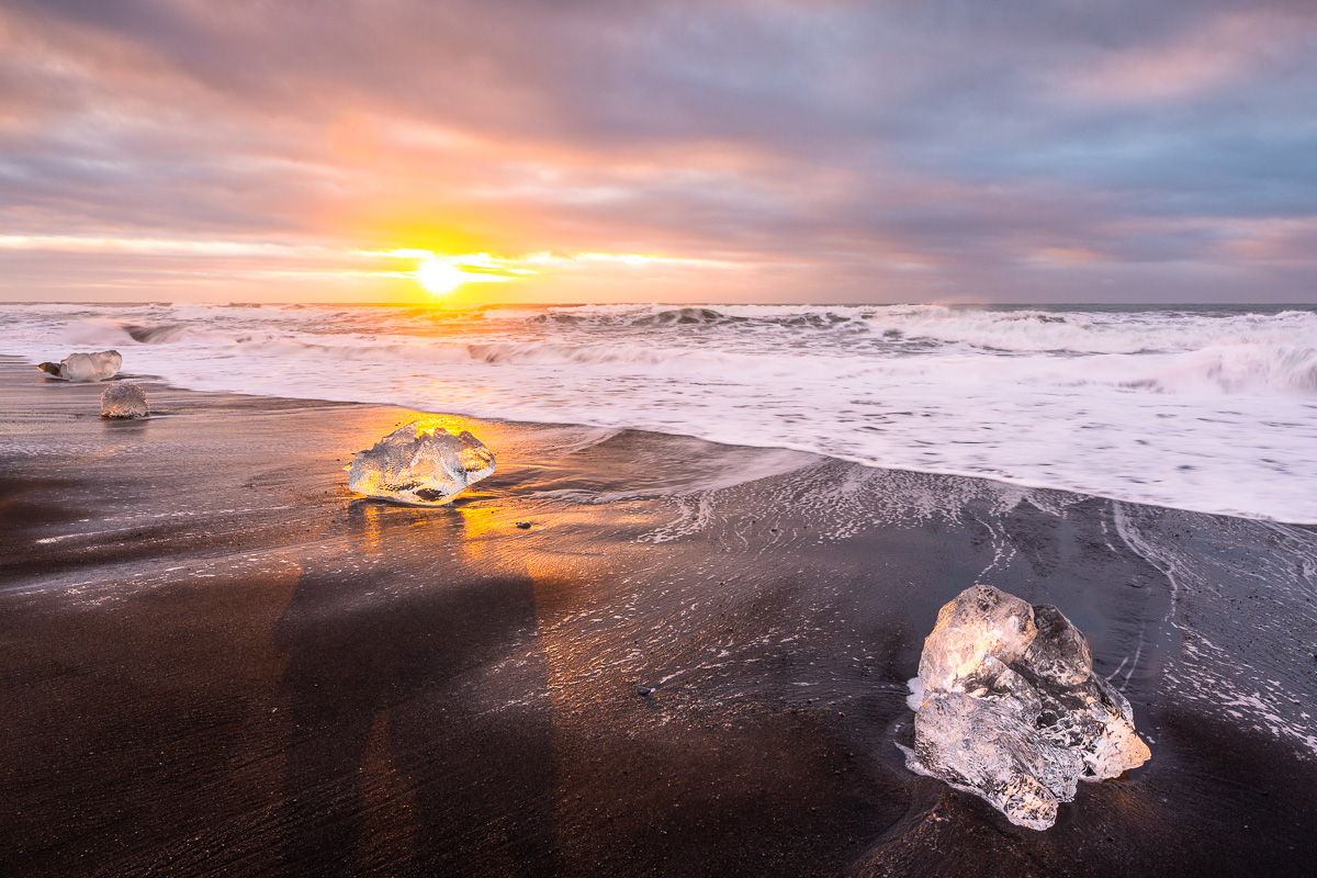 Große Eiskristalle liegen auf einem schwaren Strand